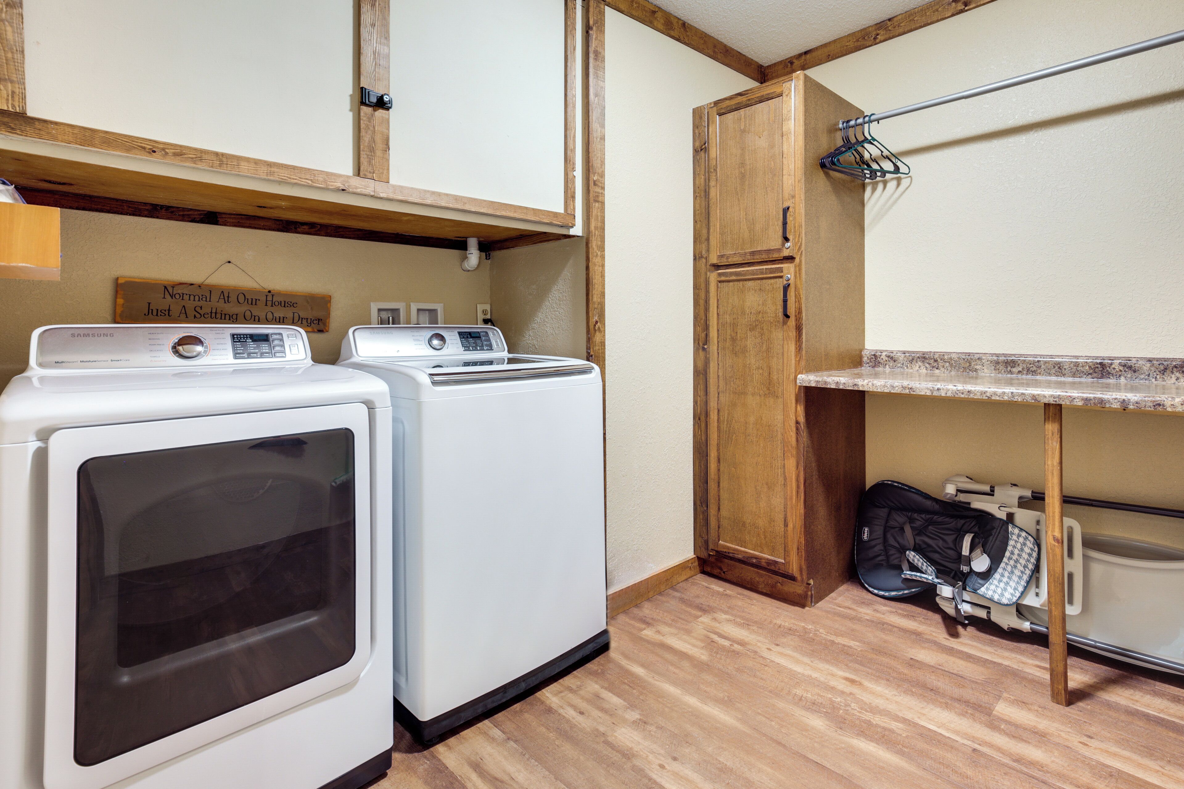 A laundry area with two white washers and dryers, wooden cabinets, and a metal drying rack.