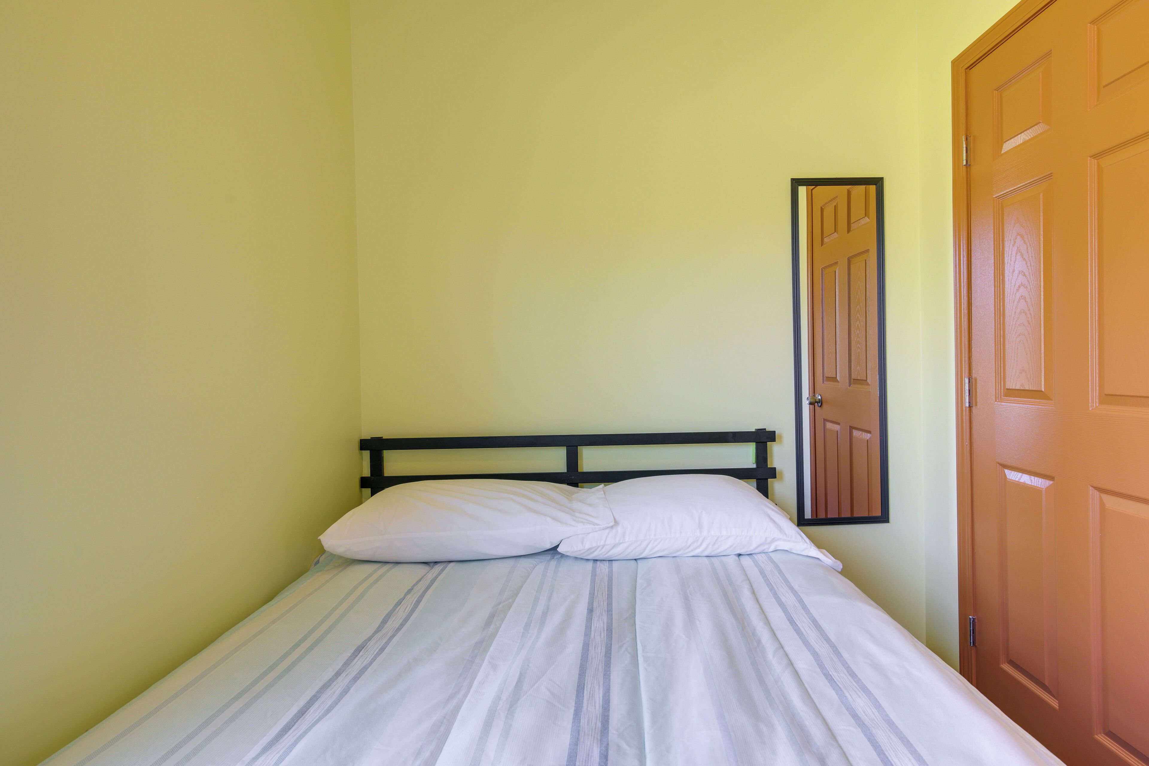 A single bed with a wooden headboard in a room with light yellow walls and a wooden door.