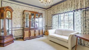 A room with a white sofa, a wooden cabinet, a guitar, and patterned wallpaper. - Historic Auburn Home w/ Theater & Yard! (Auburn)