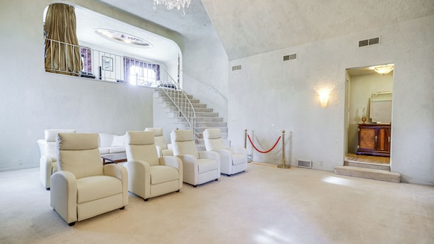 A spacious room with a curved staircase, multiple white armchairs, and a red rope barrier. - Historic Auburn Home w/ Theater & Yard! (Auburn)