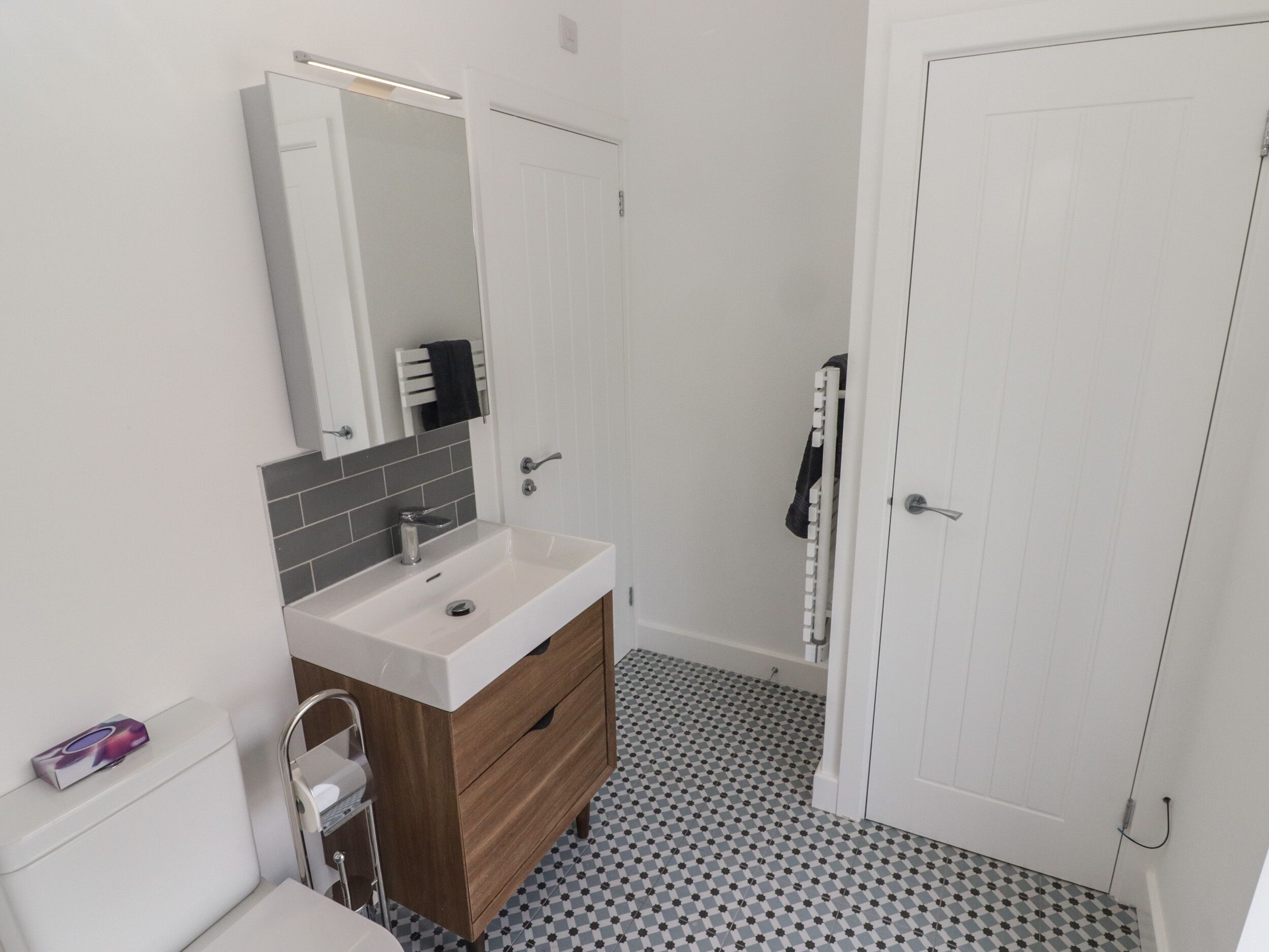 A modern bathroom with a white sink, mirror, and toilet. There is a patterned floor and a white door.