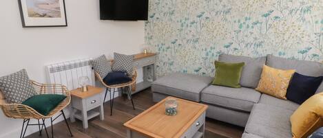 A modern living room with a grey sofa, wicker chairs, a wooden coffee table, and a TV mounted on the wall.