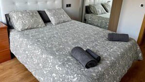 A double bed with a patterned bedspread, two pillows, and rolled towels. - Amplio apartamento cerca FIRA y Centro (L'Hospitalet de Llobregat)