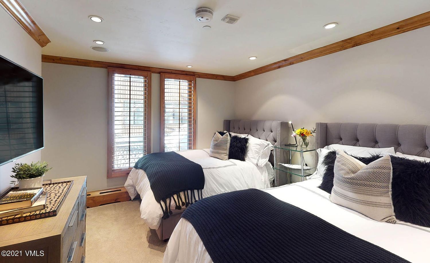 A bedroom with two beds, a bedside table with a lamp, and a window with blinds.