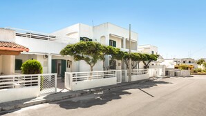 Un bâtiment moderne, de couleur blanche, doté d’un toit plat, d’une entrée sécurisée par un portail et d’une rue pavée.