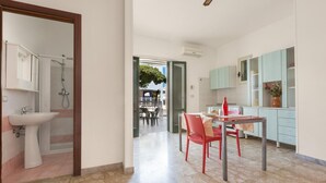A modern kitchen with light blue cabinets, a dining area with a red chair, and a bathroom with a sink and shower. - 3391 Dima Apartments - bilocale 5 by Barbarhouse (Melendugno)