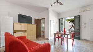 A compact living space with a red sofa, a TV on a wooden cabinet, a dining table with chairs, and a ceiling fan. - 3391 Dima Apartments - bilocale 5 by Barbarhouse (Melendugno)