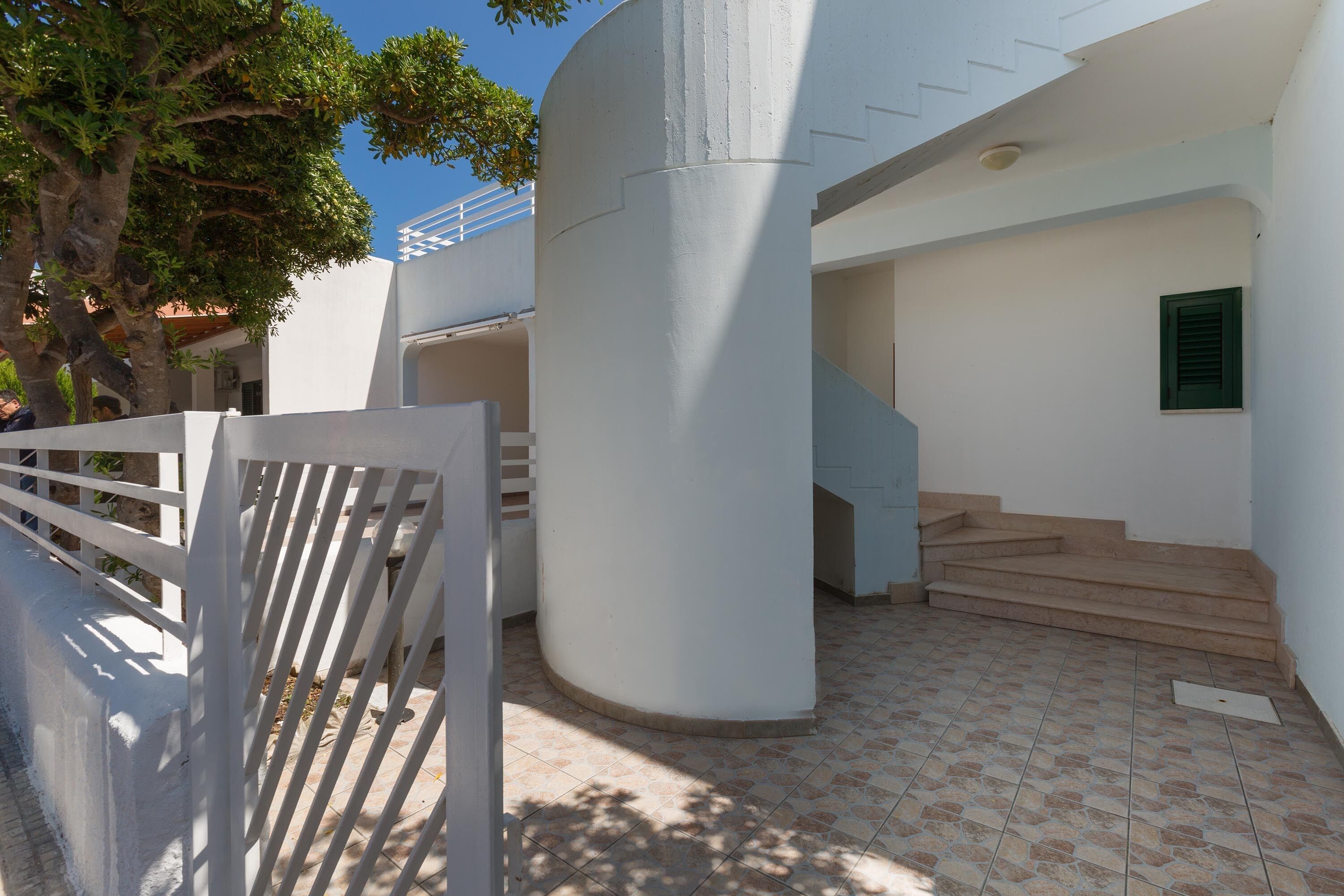 A modern building with white walls, a curved column, and a staircase leading to an upper level.