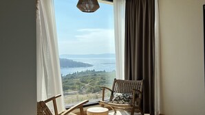 Quarto com uma cama grande, duas cadeiras de vime, uma mesa redonda pequena e vista para o mar.