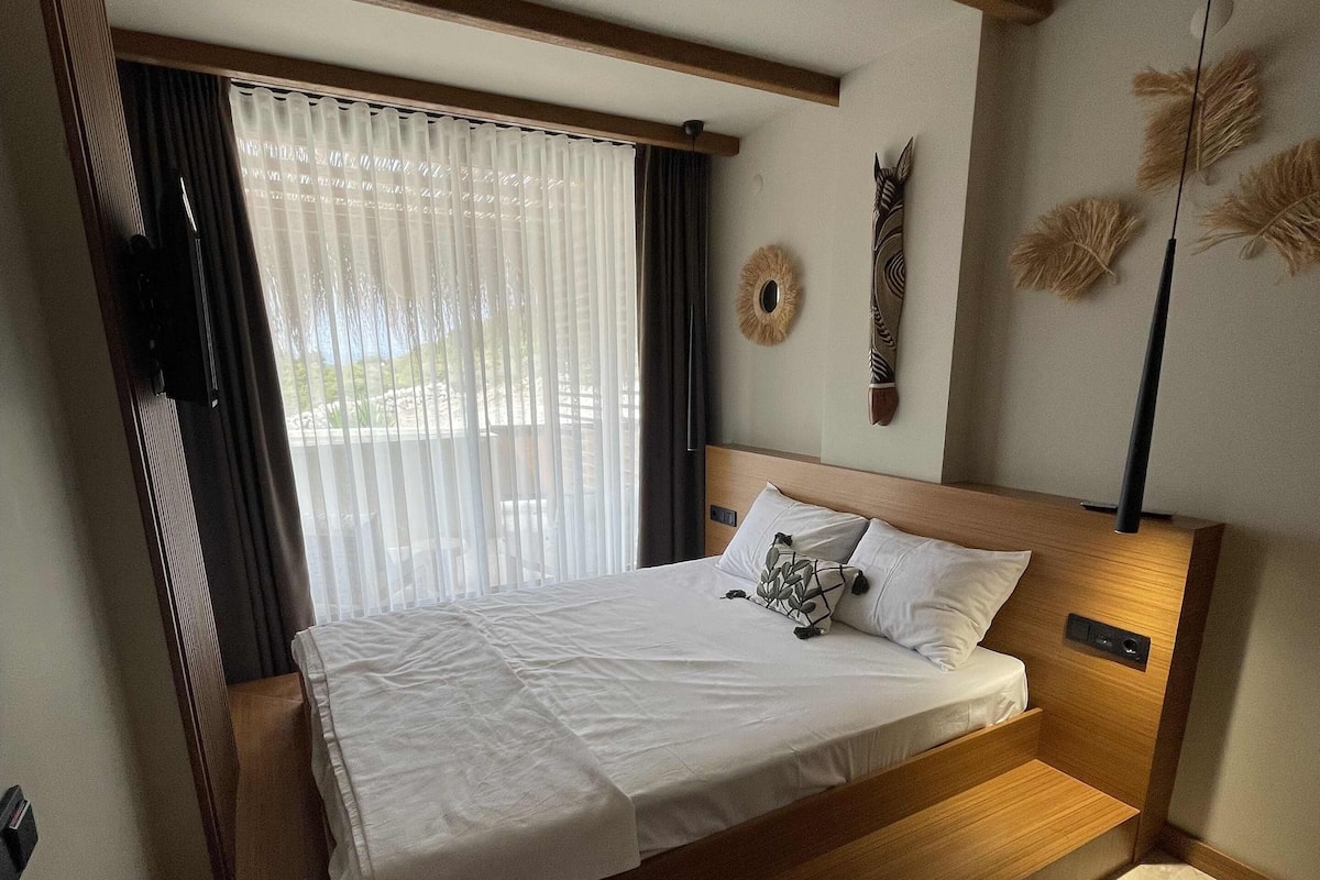 A modern bedroom with a wooden bed frame, a large window with sheer curtains, a wall-mounted decorative mirror, and a floor lamp.