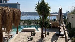 Área de piscina com vista para o mar, uma palmeira e uma espreguiçadeira.