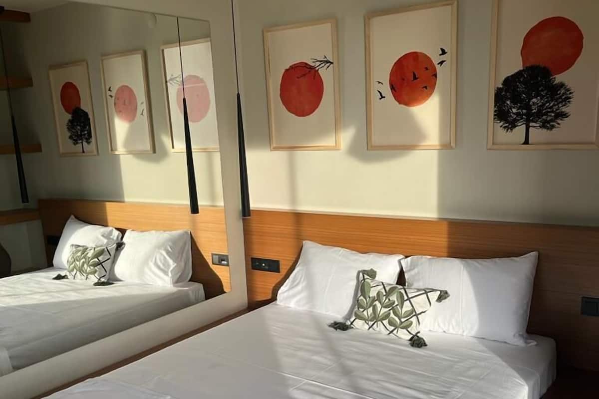A hotel room with two beds, each with white bedding and decorative pillows. The room has a wooden headboard and a large mirror on the wall.