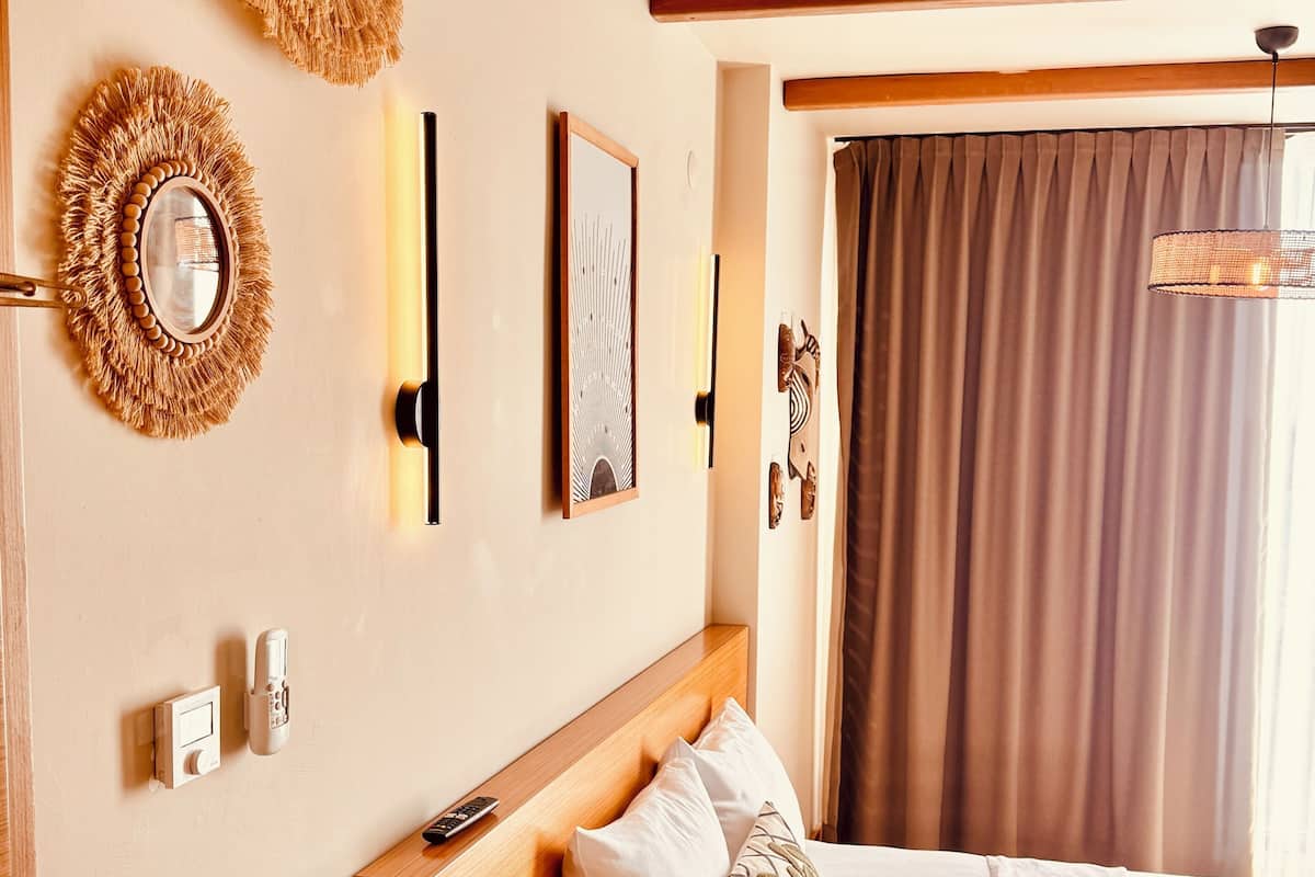 A neatly arranged bedroom with a wooden headboard, a bed with white linens, a wall-mounted mirror, and a framed picture.