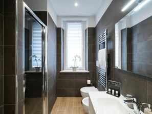 A modern bathroom with dark tiles, a white sink, and a window with a plant. - [7 min from airport] Design house with A/C and WiFi (ciampino)