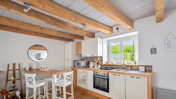 Eine moderne Küche mit weißen Schränken, Holzbalken, einem großen Fenster und einem Essbereich mit weißen Stühlen.