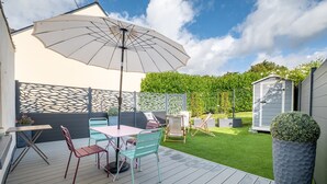 Eine Terrasse mit Tisch, Stühlen, einem großen Sonnenschirm und einem kleinen Schuppen.