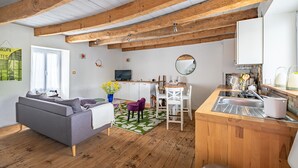 Eine moderne Küche mit Holzbalken, einem Essbereich mit einem violetten Stuhl und einem grauen Sofa.