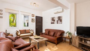 Ein Wohnzimmer mit Sofa, Sesseln, einem Couchtisch, einem Fernseher und Kunstwerken an den Wänden.
