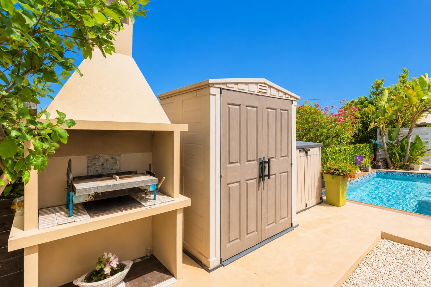 A backyard with a barbecue grill, a shed, a pool, and various plants.