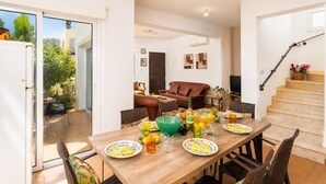 Ein Essbereich mit einem Holztisch, der für eine Mahlzeit gedeckt ist, ein braunes Ledersofa und eine Treppe, die zu einer oberen Ebene führt.