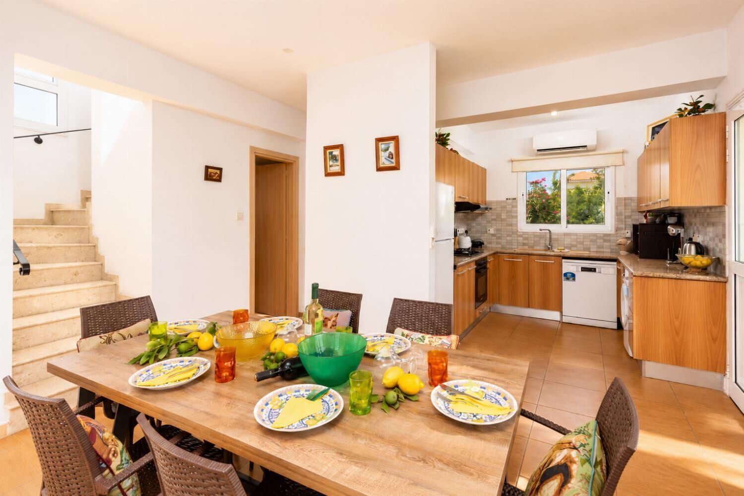 Une cuisine moderne avec des meubles en bois, un coin repas avec une table en bois et des chaises en osier, et un escalier menant à un autre niveau.