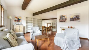 A spacious living room with a high ceiling, a dining area with wooden chairs, and a view of the kitchen through an open door. - Vigna Nuova Apartment (Firenze)
