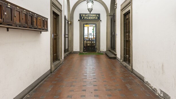 A corridor with a tiled floor, wooden cabinets on the left, and a sign reading "TRATTORIA I PARIONE" above a door. - Vigna Nuova Apartment (Firenze)