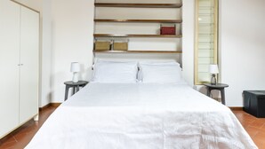 A neatly arranged bedroom with a large bed, two bedside tables with lamps, a wardrobe, and a shelf with decorative items. - Vigna Nuova Apartment (Firenze)