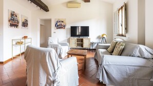A living room with a TV, sofa, and chairs, a wooden ceiling beam, and artwork on the walls. - Vigna Nuova Apartment (Firenze)