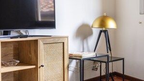 A room with a television on a wooden cabinet, a small table with a lamp, and a wall socket. - Vigna Nuova Apartment (Firenze)