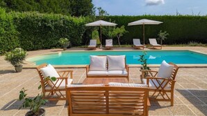 A pool area with lounge chairs and umbrellas, surrounded by a hedge and potted plants.