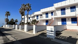 Un edificio costero con paredes blancas y contraventanas azules, que cuenta con balcones y una escalera.