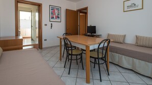 Una habitación con una cama, un sofá, una mesa de comedor con sillas, un televisor y una puerta que da a otra habitación.
