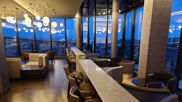 A modern bar area with a long counter, multiple seating options, and large windows offering a city view. - Lux Corner Unit-spa-gym-office-lounges (Montréal)