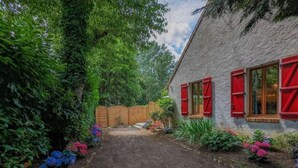 A stone building with red shutters, a wooden fence, and a garden with various flowers. - "Le Clos de la Reine", Maison Avec Piscine (Josnes)