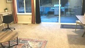 A room with a large sliding glass door leading to a backyard, a desk, a chair, and a rug. - WFH Private Suite kitchen & Yard (Sparks)