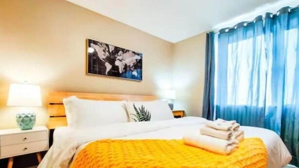A hotel room with a bed, a nightstand, a lamp, a world map on the wall, and blue curtains. - WFH Private Suite kitchen & Yard (Sparks)