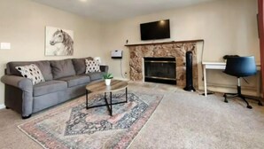 A living room with a sofa, a coffee table, a fireplace, a mounted TV, and a desk with a chair. - WFH Private Suite kitchen & Yard (Sparks)