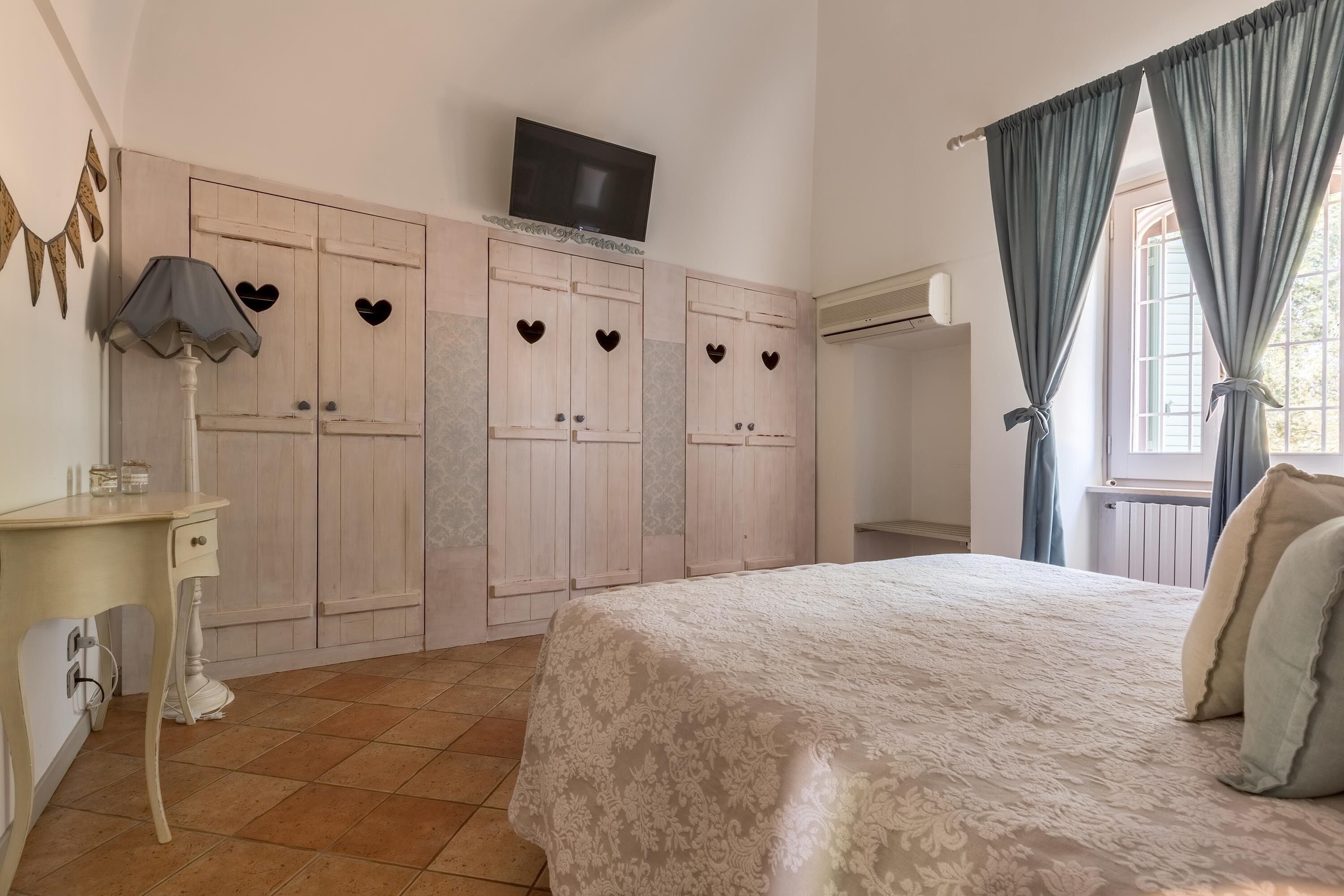 A bedroom with a bed, wardrobe, TV, and curtains.