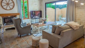 Un salon chaleureux avec une cheminée, un téléviseur et une grande fenêtre donnant sur un jardin.