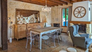 Un intérieur rustique avec un mur en pierre, des poutres en bois, un lustre, une table à manger avec des chaises et une cheminée.