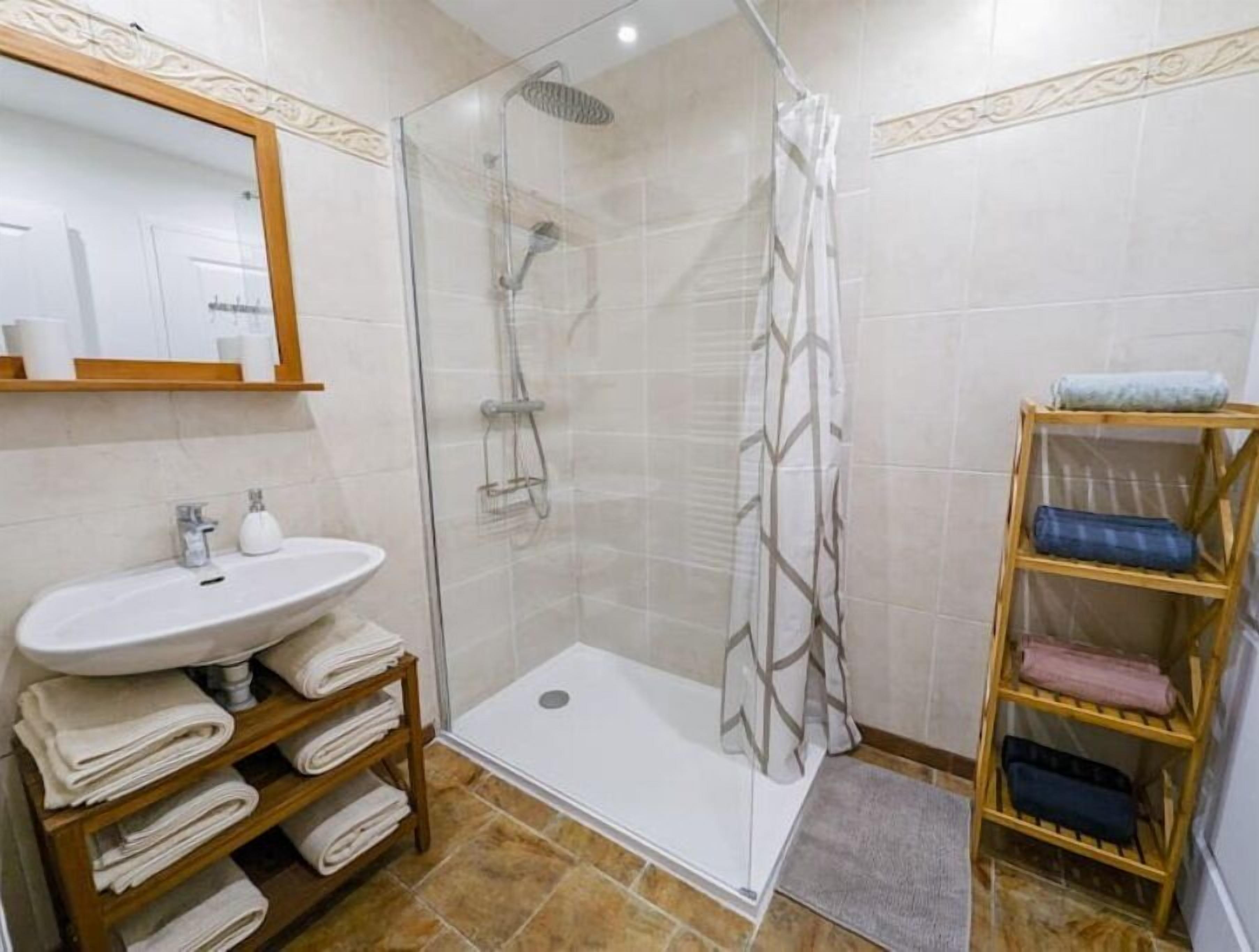 A bathroom with a glass-enclosed shower, a sink with a mirror above it, and a towel rack with folded towels.