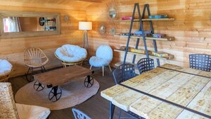 L’intérieur chaleureux d’un chalet, avec un décor en bois, une table à manger, des chaises, une lampe et des étagères remplies de livres.