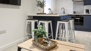 A modern kitchen with a built-in oven, a sink, and bar stools. - Llety Pen Deitsh 2 (Caernarfon)