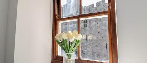 A window with a view of a stone building, a clear glass vase with white flowers on a white ledge.