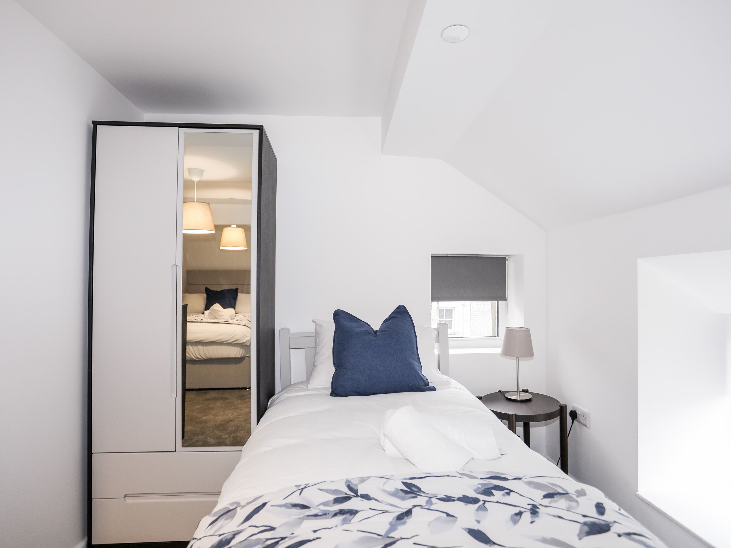 Un dormitorio con cama, armario, mesita de noche y ventana.