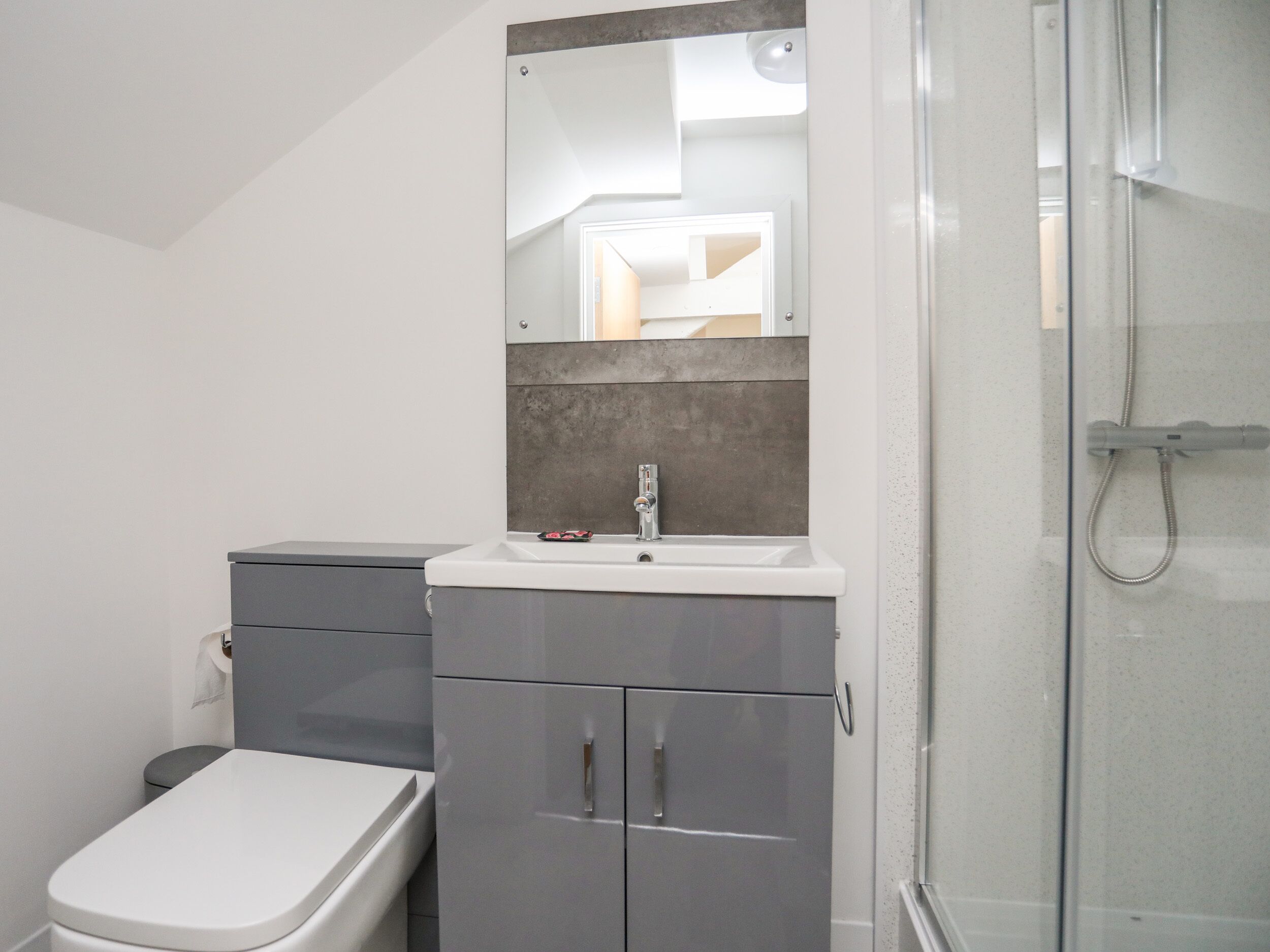 A modern bathroom with a toilet, a sink with a mirror, and a shower area.