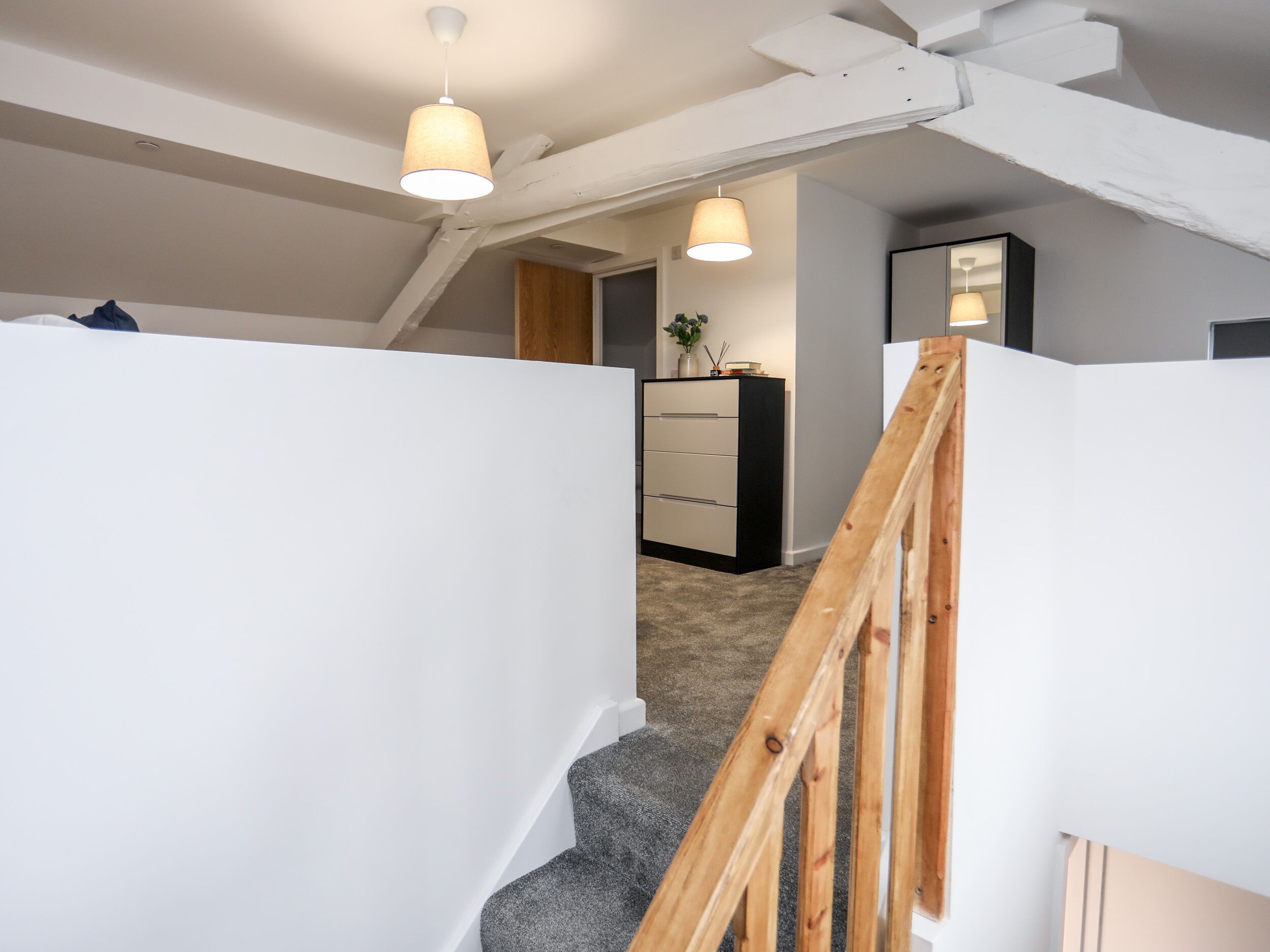 A staircase with wooden handrails and a carpeted landing. There are pendant lights hanging from the ceiling.