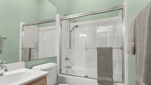 Een badkamer met een douche met glazen wand, een wit toilet en een wastafel met spiegel.