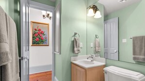 Een badkamer met een houten wastafelmeubel, een witte wastafel en een toilet. Er hangt een schilderij van rozen aan de muur en een spiegel boven de wastafel.
